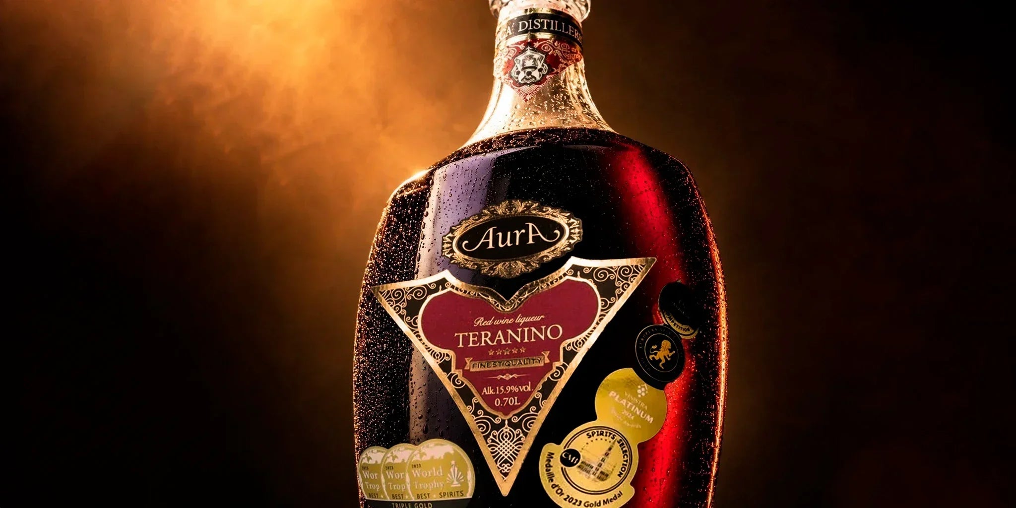 Aura Teranino Croatian red wine liqueur bottle close-up with award medals, deep ruby color and warm dramatic lighting, styled as a premium European liqueur for elegant sipping and gifting.