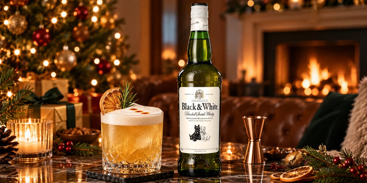 Black & White Blended Scotch Whisky 40% 0.7L bottle served with a festive whisky cocktail beside a glowing fireplace, Christmas tree, candles and holiday decorations.
