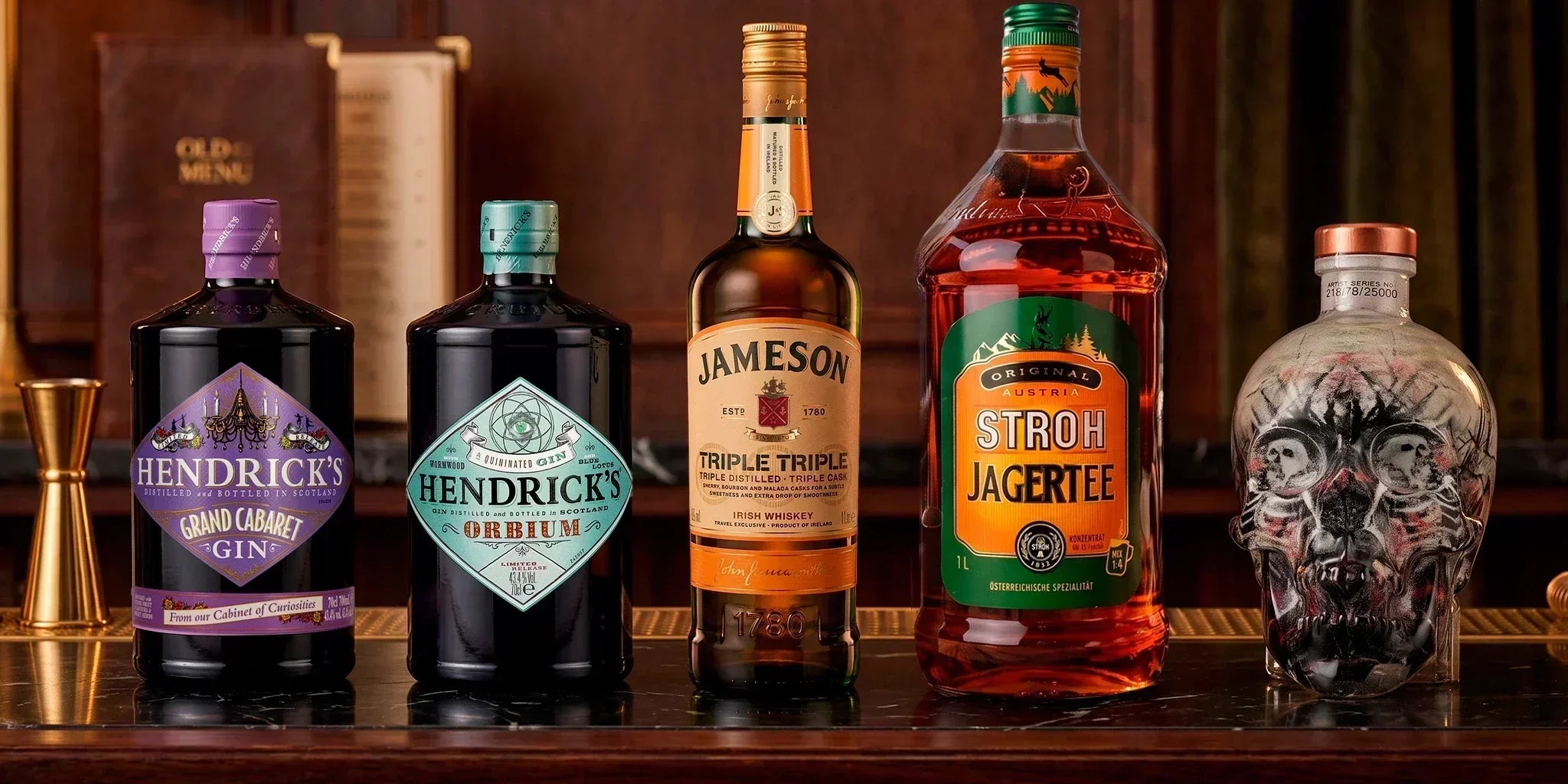 Premium spirits selection with Hendrick’s Grand Cabaret Gin, Hendrick’s Orbium, Jameson Irish Whiskey, Stroh Jagertee and a skull-shaped bottle on a dark bar counter.