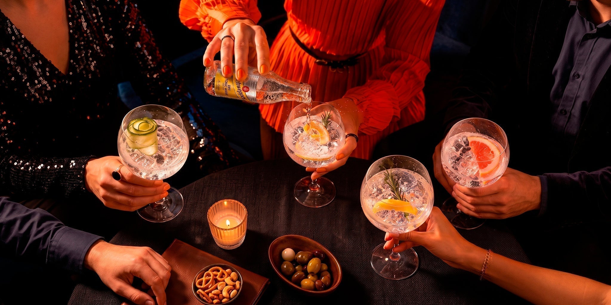 Schweppes Dry Tonic Water being poured into gin and tonic cocktails at an elegant evening party with friends, garnishes and snacks.
