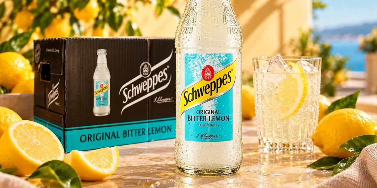 Schweppes Original Bitter Lemon 24x200ml bottles with chilled glass, fresh lemons and branded case in a bright Mediterranean-style setting.