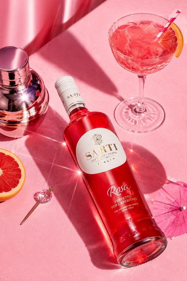 Sarti Rosa pink Italian aperitivo bottle with a bright grapefruit cocktail, ice, cocktail shaker and pink summer styling.